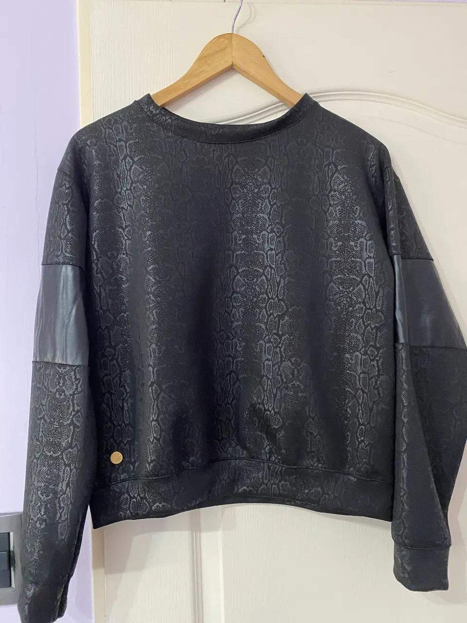 Buzo de cuello redondo negro con estampado de piel de serpiente. Detalles de cuero sintético en los hombros. Ideal para un look casual y moderno.