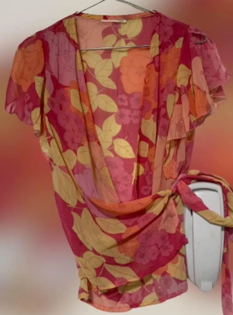 Blusa de gasa con estampado floral en tonos rojos, rosas y amarillos. Diseño envolvente con mangas cortas con volados y lazos para ajustar en la cintura. Ideal para un look femenino y fresco.