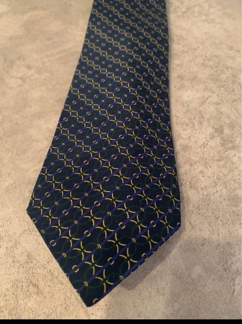 Corbata  azul marino con un patrón geométrico en tonos amarillos y verdes. Ideal para complementar un look formal o de trabajo.