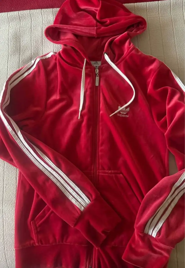 Buzo Adidas rojo de terciopelo con cierre y capucha. Detalles de las tres tiras blancas en las mangas y logo bordado. Ideal para un look deportivo y cómodo.