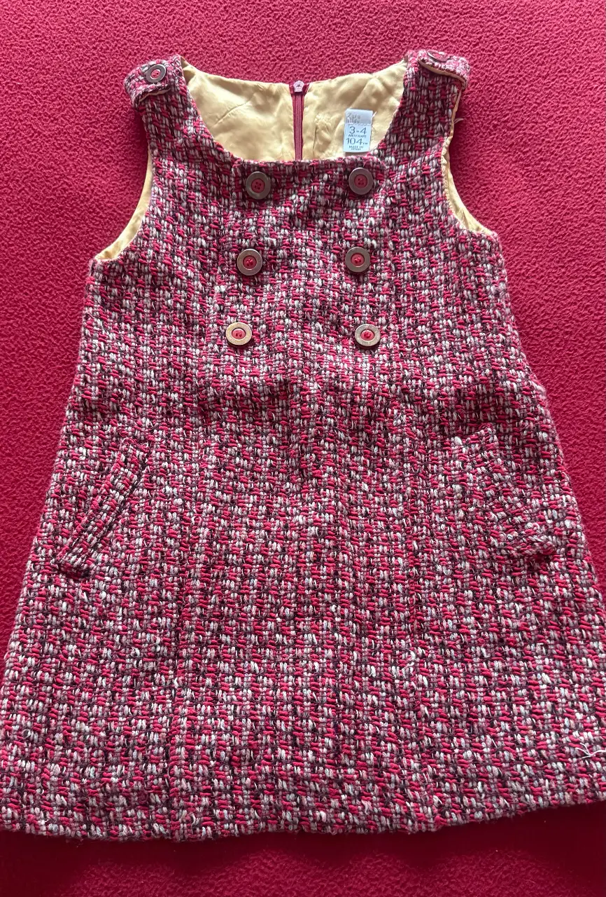 Vestido de niña, de tela tipo tweed en tonos rojos y blancos. Tiene un diseño con botones en la parte delantera y bolsillos. Ideal para un look casual y abrigado.totalmente forrado y con cierre