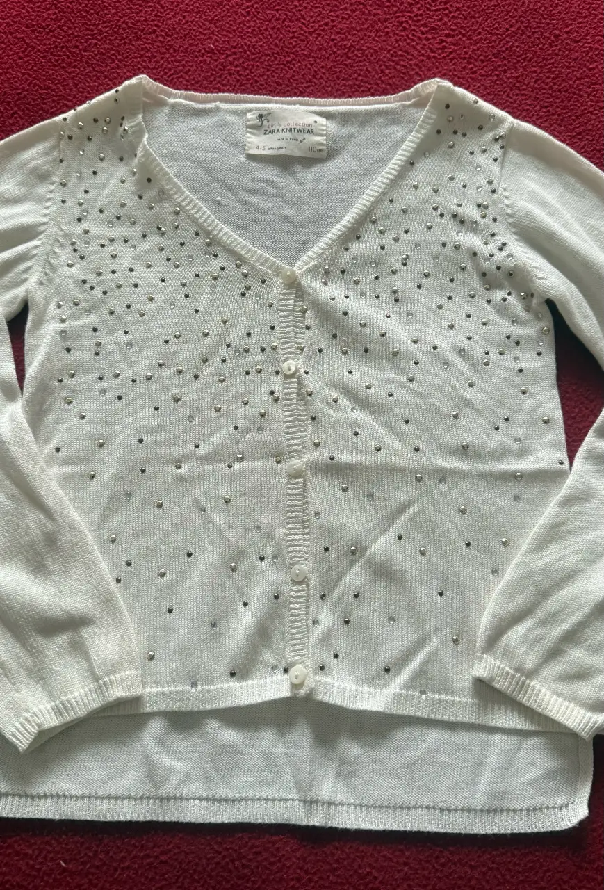 Cardigan blanco de niña, tejido con detalles de brillos plateados. Ideal para ocasiones especiales.