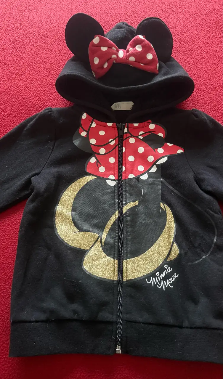 Buzo con cierre para niña, con diseño de Minnie Mouse. Tiene capucha con orejas y moño rojo con lunares blancos e interior con corderito. Ideal para un look casual y divertido.talle 6/8