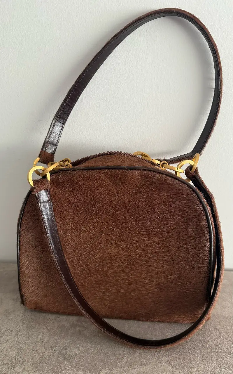 Cartera de mano  de cuero con pelo marrón. Detalles dorados y cierre superior. Sarkany impecable