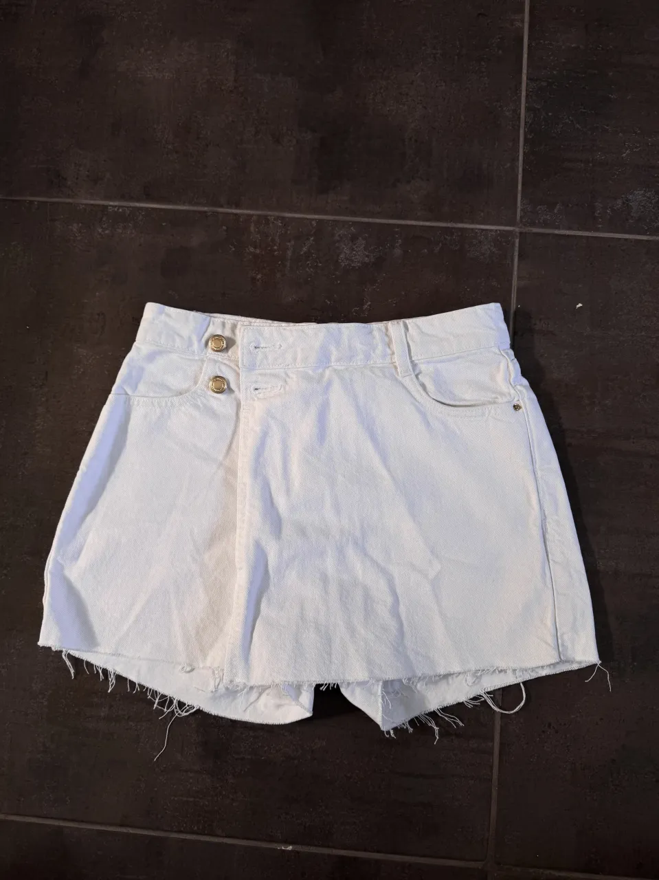 Shorts de jean blancos con roturas en los bordes inferiores. Tienen doble botón en la cintura y bolsillos.