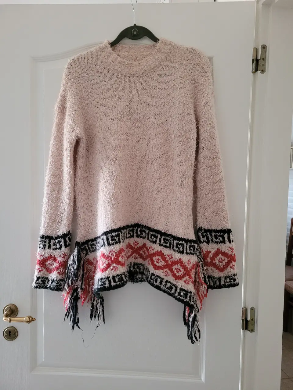 Sweater largo de tejido grueso en color rosa, con detalles en negro y rojo en el borde inferior. Ideal para un look casual y abrigado.