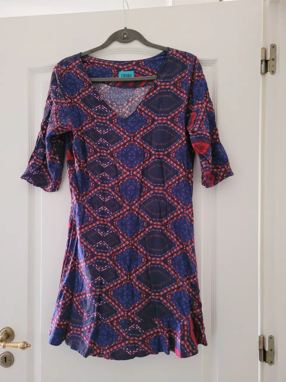 Vestido midi con estampado geométrico en tonos azules y rojos. Corte en V y mangas 3/4. Ideal para un look casual y cómodo.