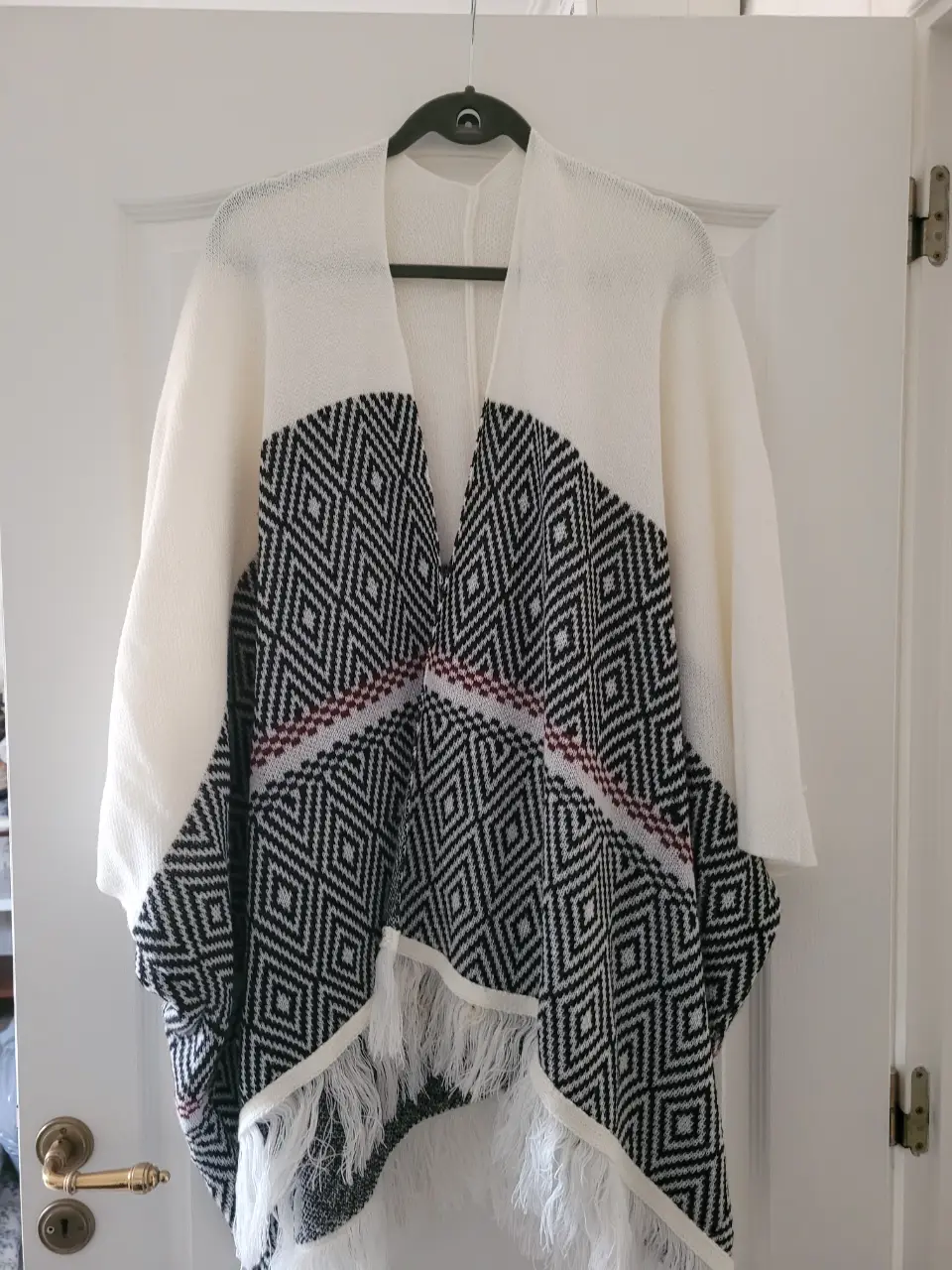 Kimono/poncho de lana con diseño geométrico en blanco y negro, ideal para un look bohemio y casual. Con flecos en el borde inferior, perfecto para usar en invierno.
