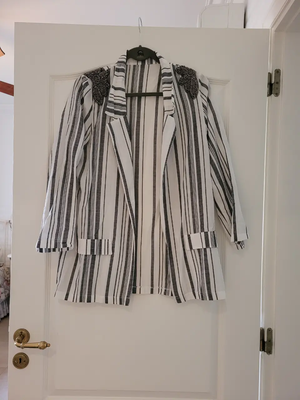 Blazer a rayas blanco y negro con detalles de pedrería en los hombros. Ideal para un look elegante y moderno.