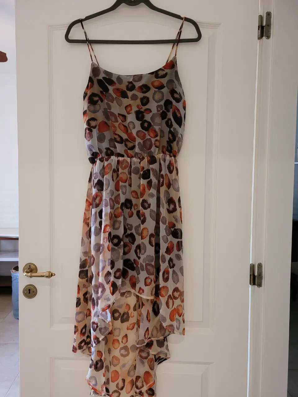 Vestido midi  de fiesta hecho en gasa con estampado de lunares en tonos marrones y naranjas. Diseño con tirantes finos y falda asimétrica con volados. Ideal para un look fresco y moderno.