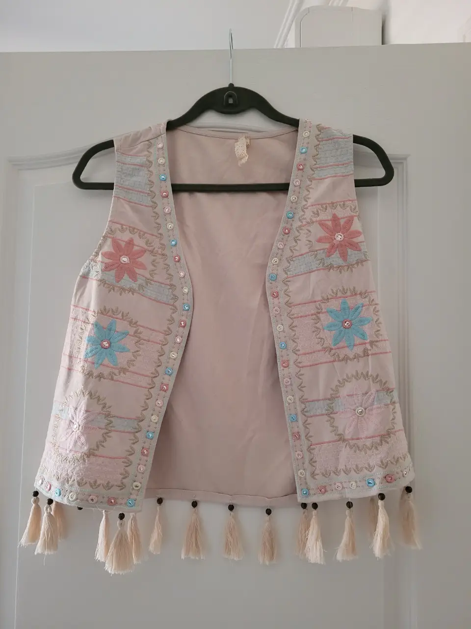 Chaleco de mujer estilo boho, con bordados florales en tonos rosa y celeste. Detalles de cuentas y borlas en el borde inferior. Ideal para un look casual y con onda.
