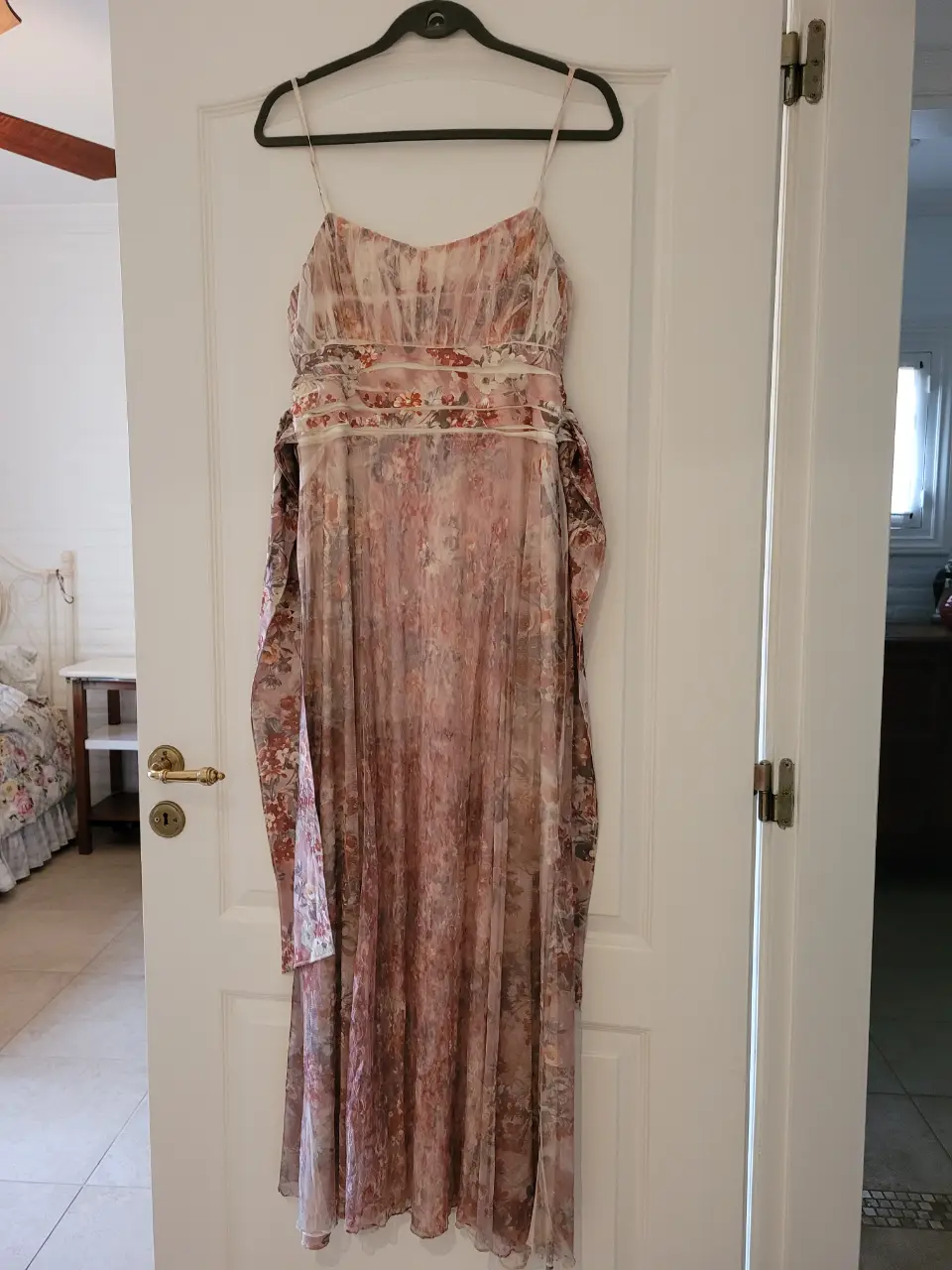 Vestido largo de fiesta con estampado floral en tonos rosados y detalles plisados. Incluye cinturón y lazos para ajustar abajo del busto.  Ideal para eventos especiales.