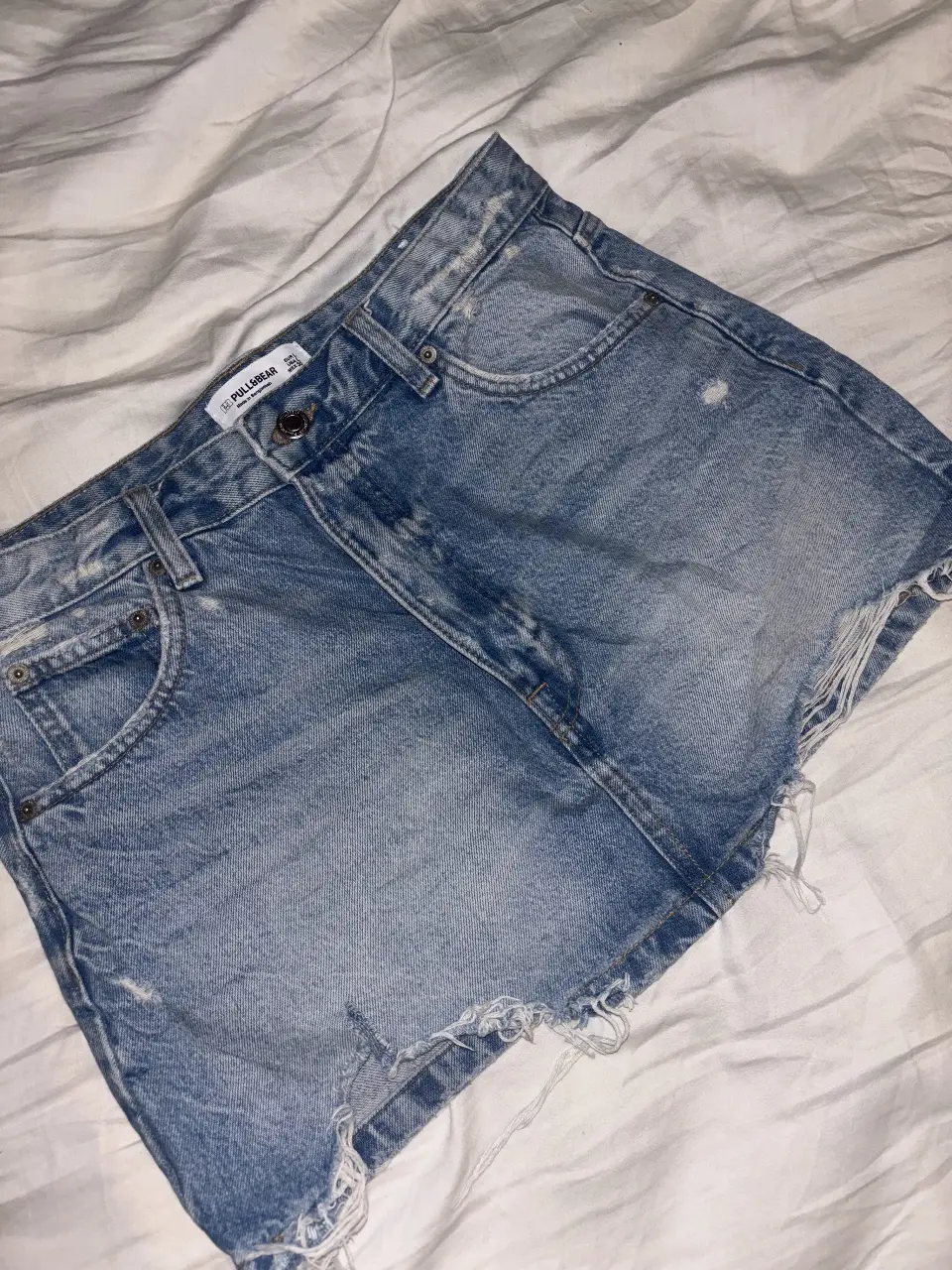 Short de jean azul claro de la marca Pull&Bear, con detalles rotos y corte desflecado. Talle L, ideal para un look casual y moderno.