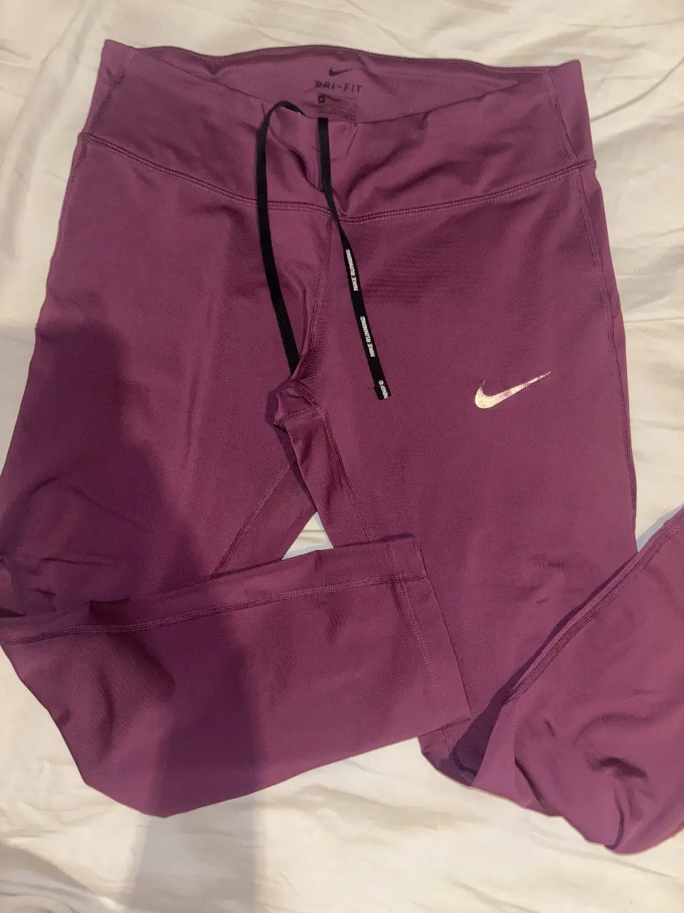 Calzas deportivas Nike Dri-FIT para mujer, color violeta. Con cintura alta y cordón ajustable. Ideal para running y entrenamiento.