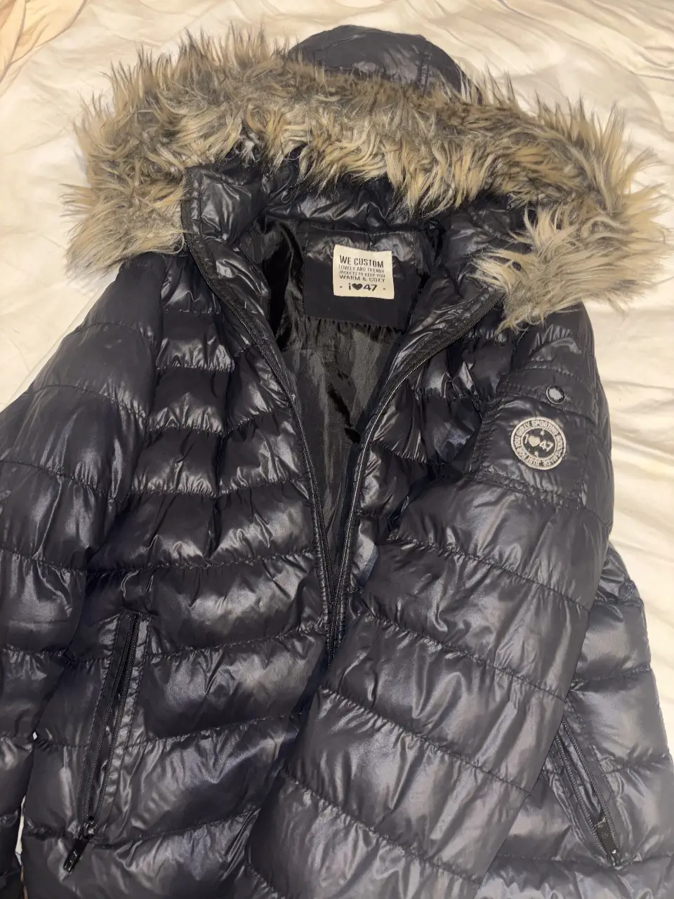 Campera de pluma negra con capucha y borde de piel sintética. Ideal para el invierno, con cierre y bolsillos. Marca  47 street