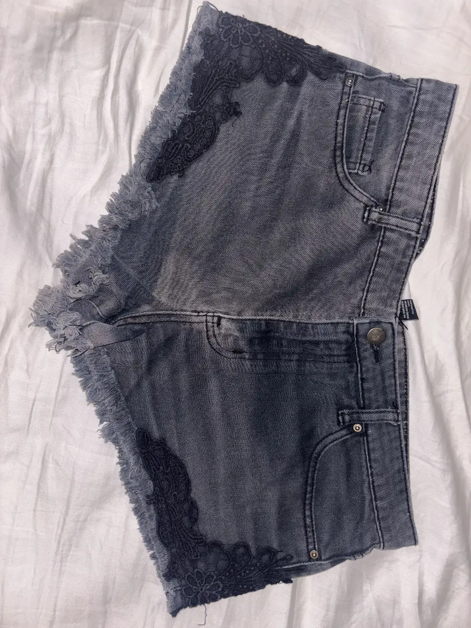 Short de jean gris con detalles de encaje negro en los bordes. Talle 30 de Forever 21. Ideal para un look casual y moderno. Estilo gastado.