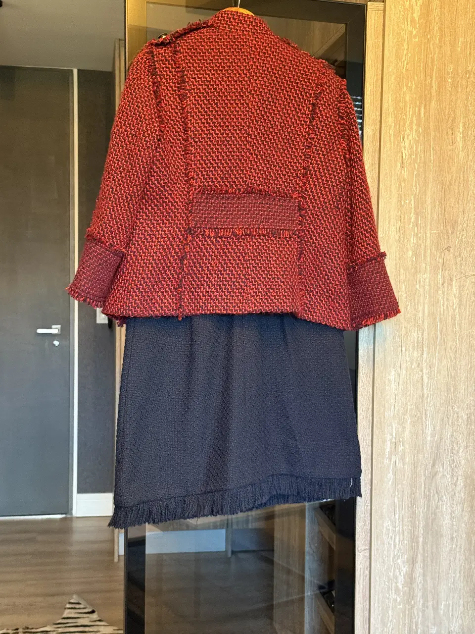 Conjunto de blazer y pollera de tweed rojo y negro. El blazer tiene botones negros y detalles desflecados. La pollera es de color negro con flecos en el borde.