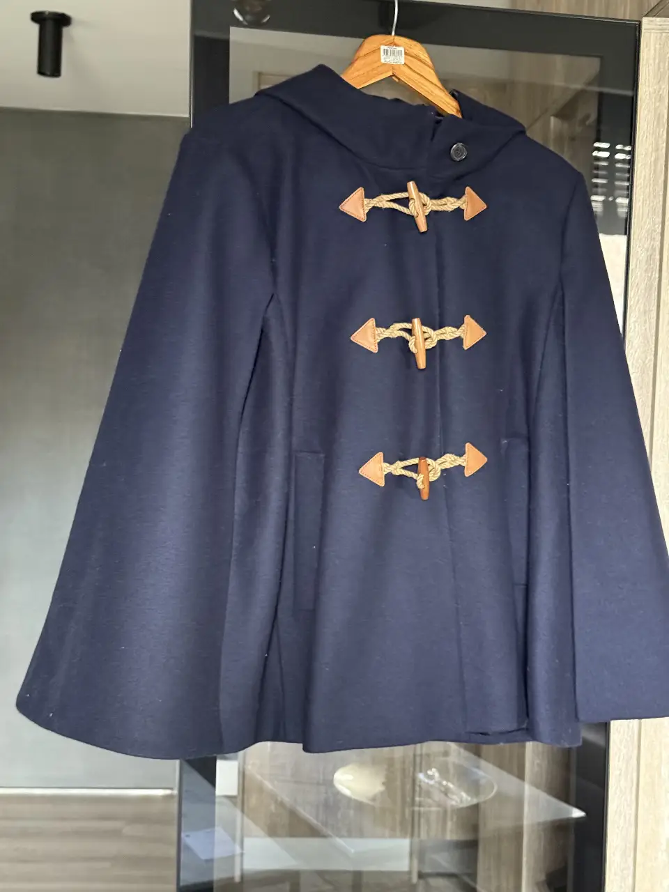 Preciosa capa azul marino con capucha y detalles de madera. Ideal para un look elegante y abrigado en invierno. Perfecta para combinar con diferentes outfits.