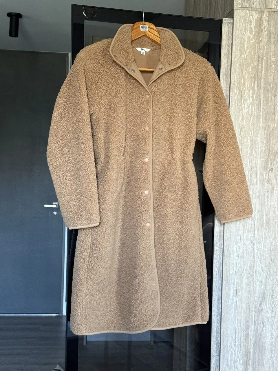 Tapado largo de mujer, color marrón claro, estilo teddy, con cuello solapa y cierre con botones. Ideal para el invierno, de la marca Uniqlo.
