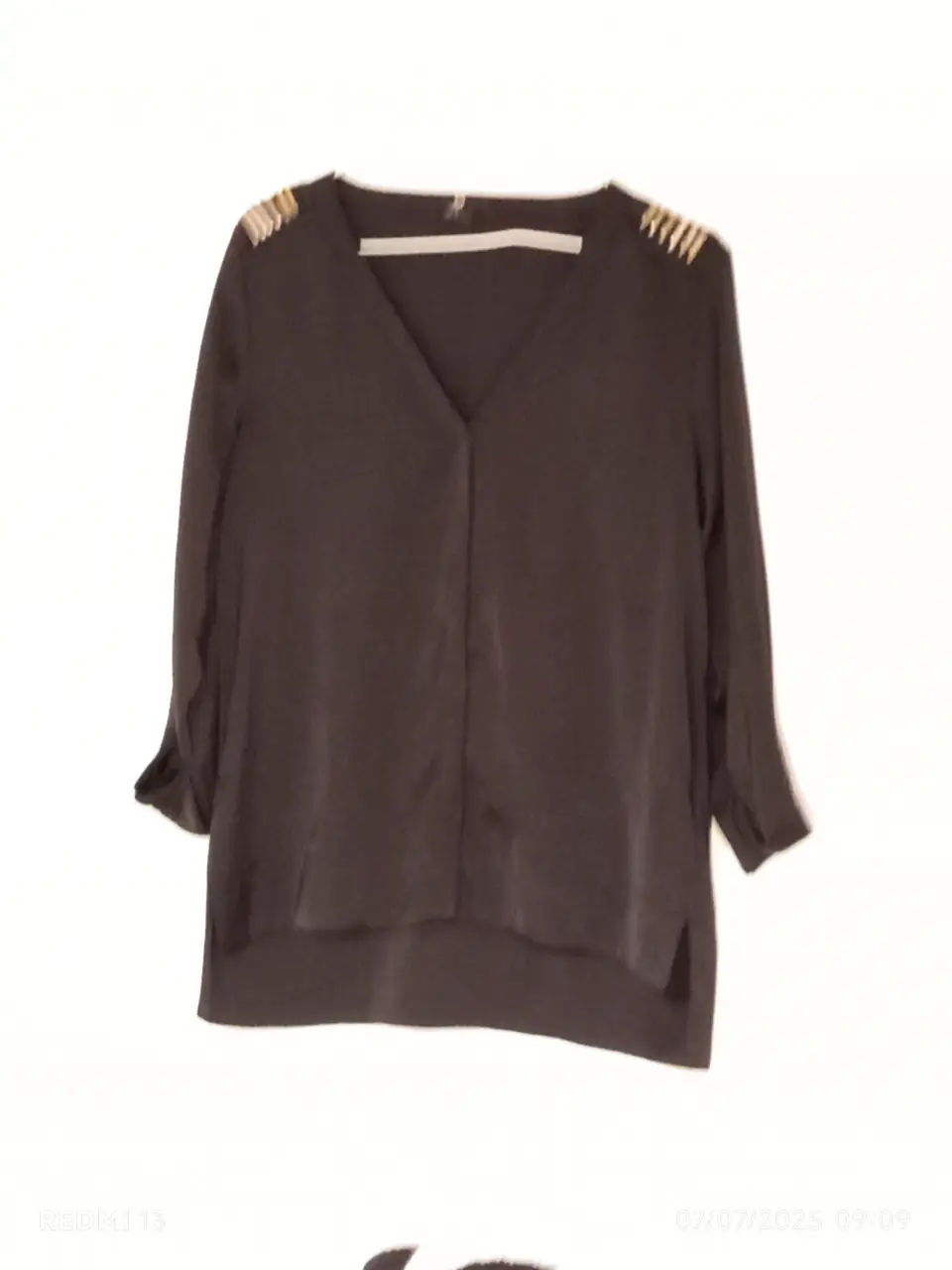 Blusa negra HYM con detalles dorados en los hombros, manga larga y cuello en V. Ideal para un look elegante y versátil.