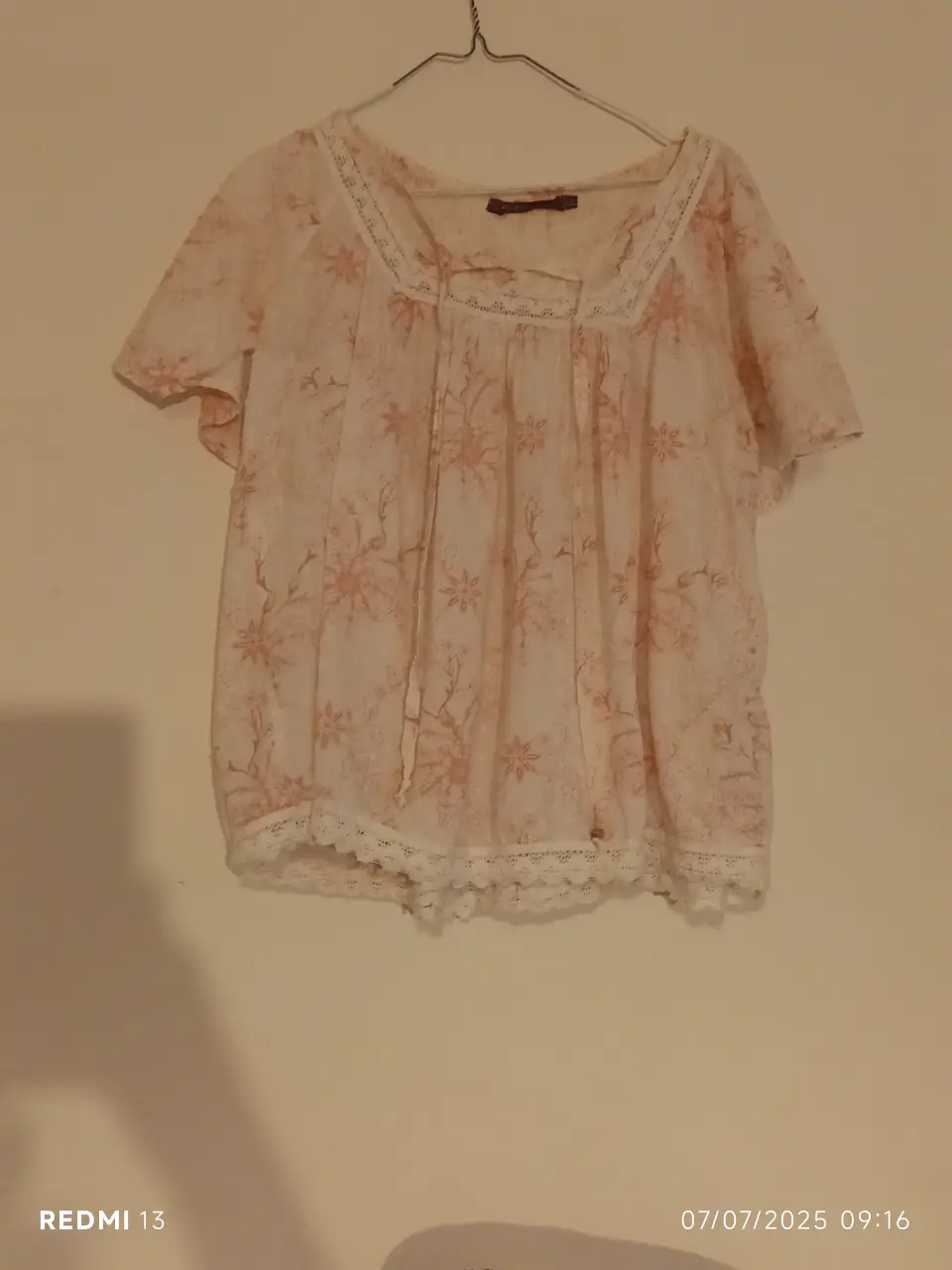 Blusa de mujer con estampado floral en tonos rosa y blanco, con detalles de encaje en el cuello y el borde inferior. Ideal para un look casual y romántico.