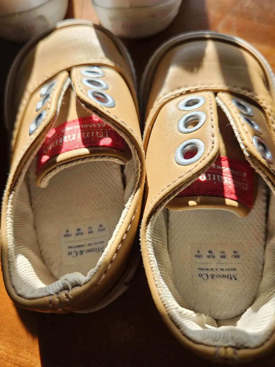 Zapatillas de bebé color marrón claro, estilo casual, con detalles de ojales y etiqueta en el interior. Ideales para un look cómodo y moderno.