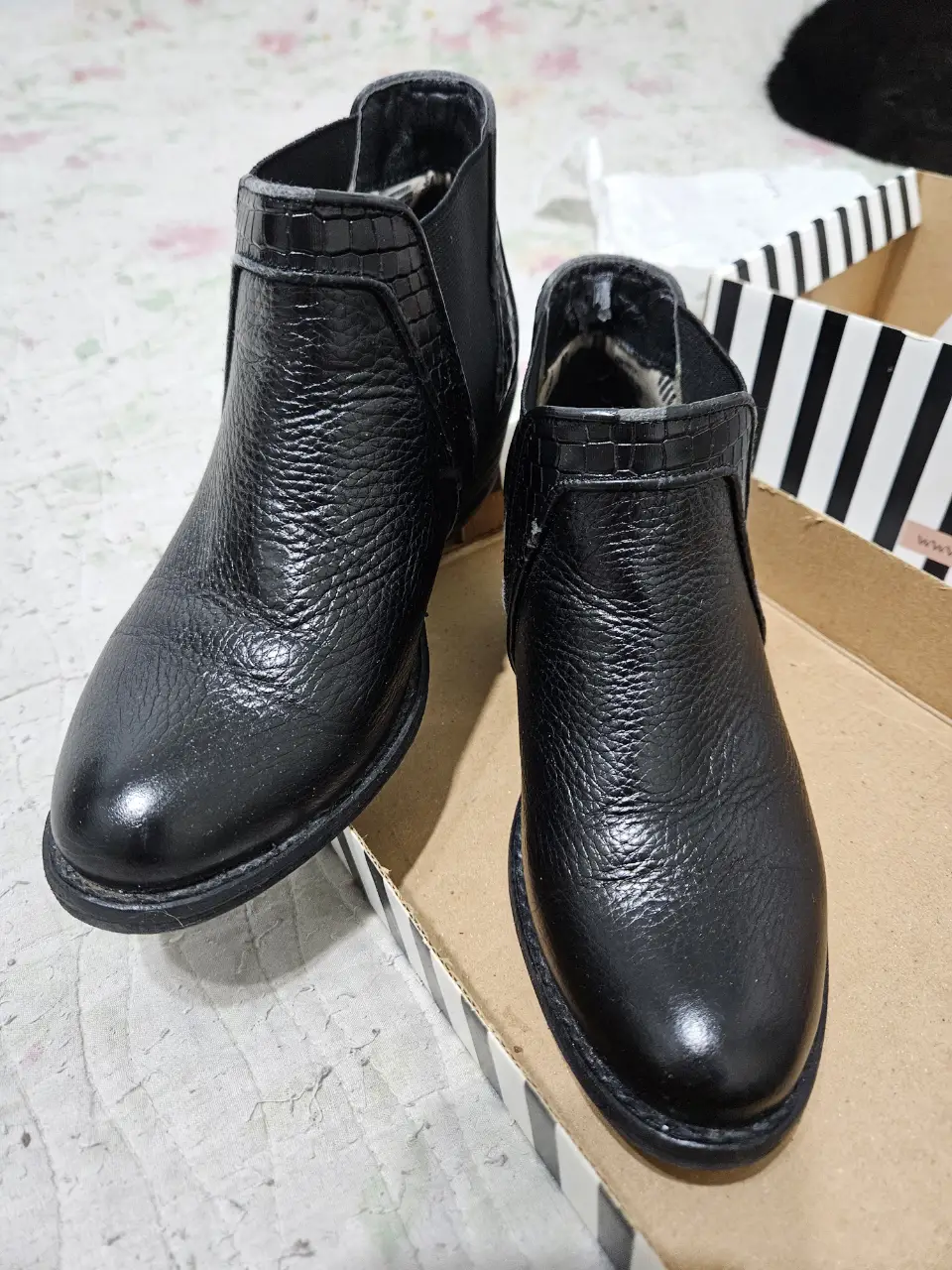 Botines negros de cuero, con detalles de textura tipo reptil en la parte superior y laterales. Diseño elegante y versátil, ideales para combinar con diferentes outfits.