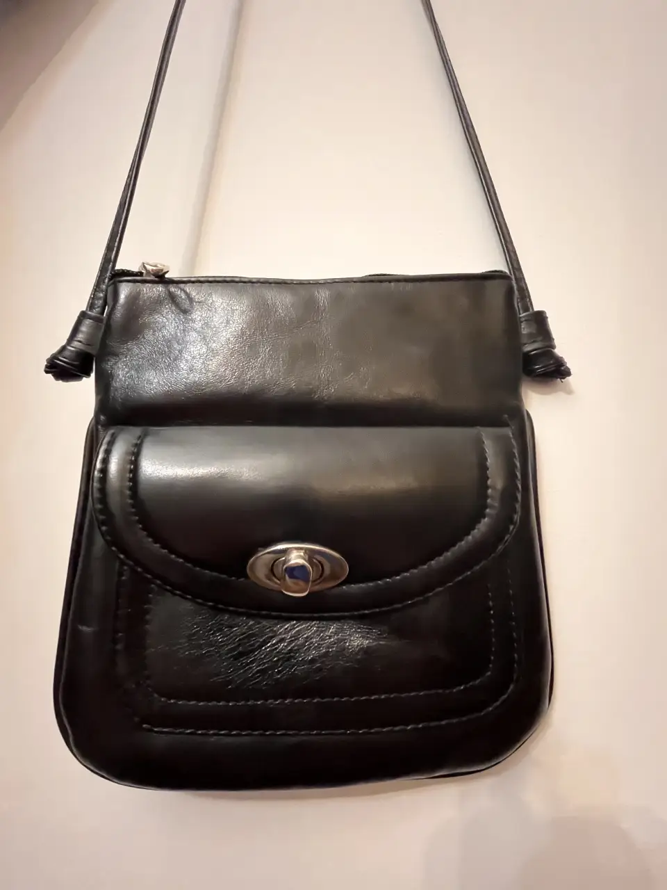 Bandolera negra de cuero vacuno con solapa y cierre metálico. Ideal para llevar lo esencial con estilo.