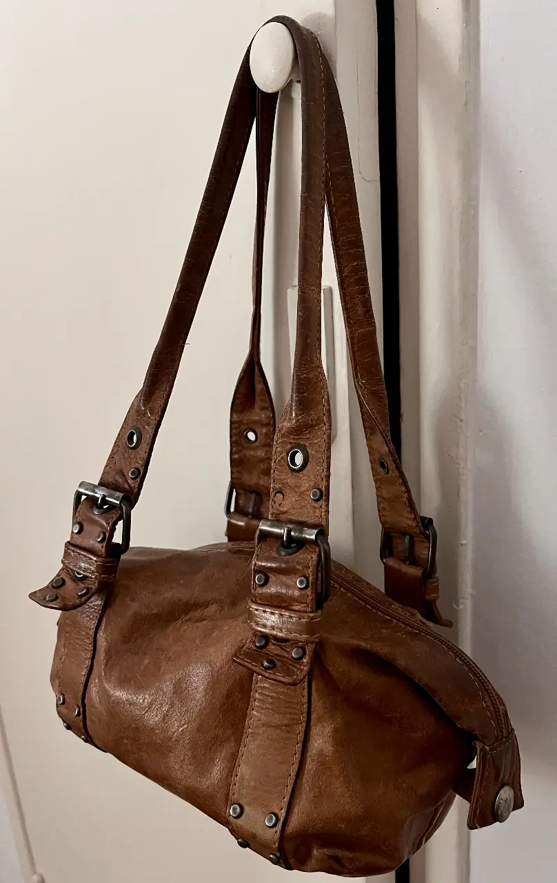 Cartera marrón de cuero con detalles de hebillas y tachas. Ideal para un look casual y con estilo. Diseño de autor, Palermo Soho.