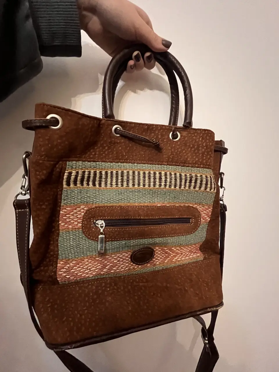 Cartera de hombro artesanal de gamuza marrón con detalles tejidos en la parte frontal. Posee un bolsillo con cierre y correa ajustable. Cuero de vaca y carpincho.