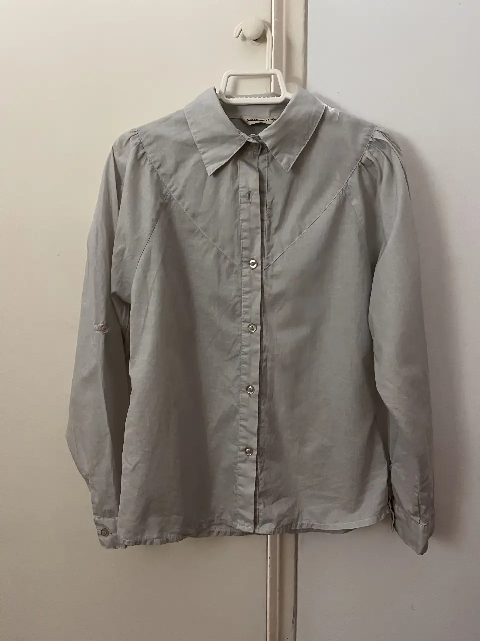 Blusa gris de manga larga con detalles en los hombros y botones. Ideal para un look casual y elegante.
