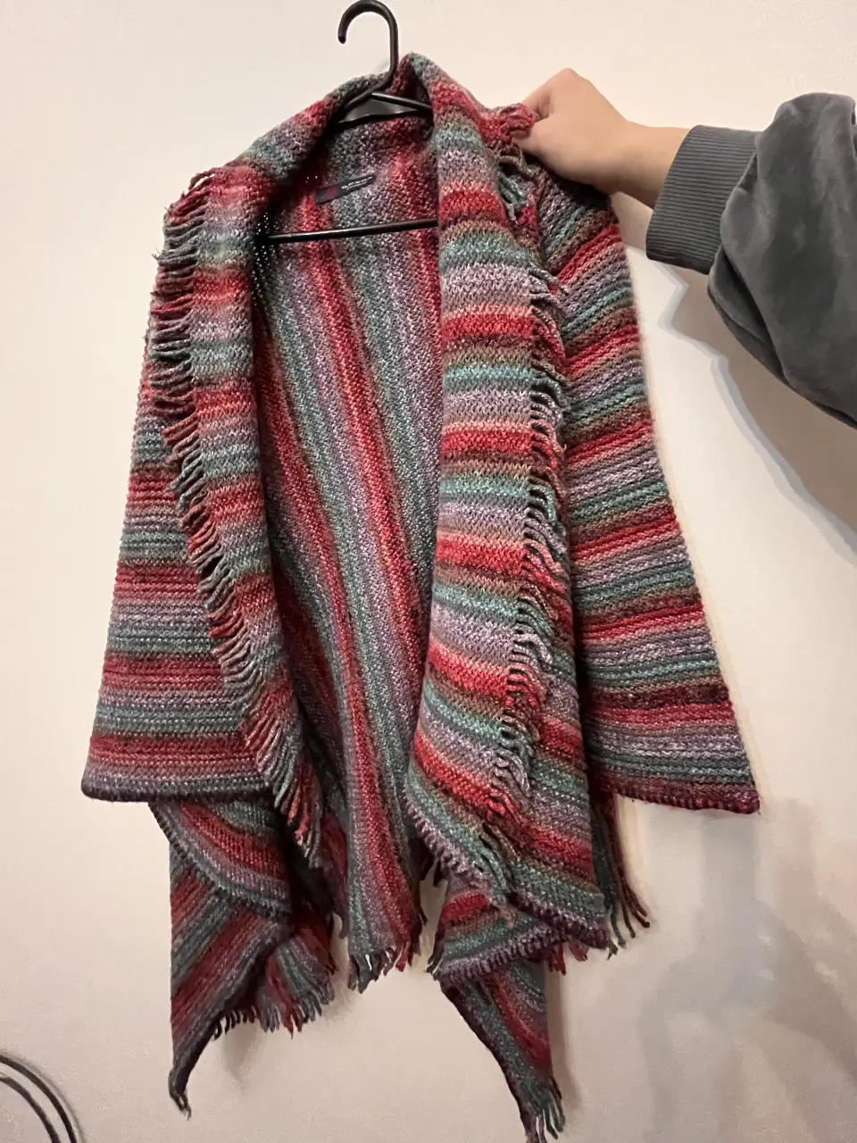 Cardigan tejido a rayas en tonos rojos, grises y verdes. Con flecos en los bordes y un diseño envolvente, ideal para un look bohemio y abrigado. Sin uso.