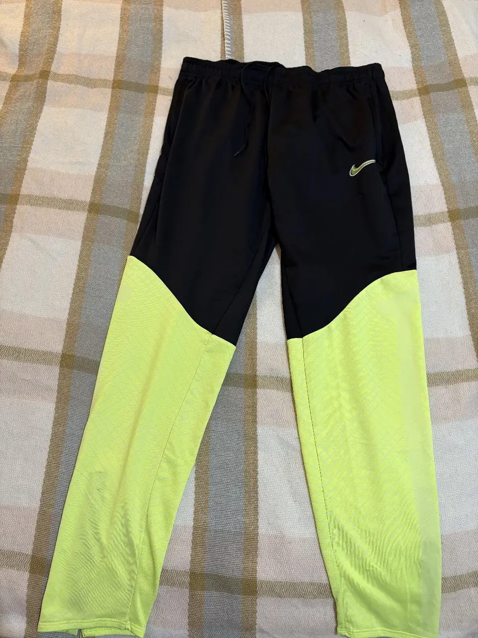 Pantalón deportivo Nike de hombre, negro con detalles en amarillo flúor. Ideal para entrenar o para un look casual y cómodo.