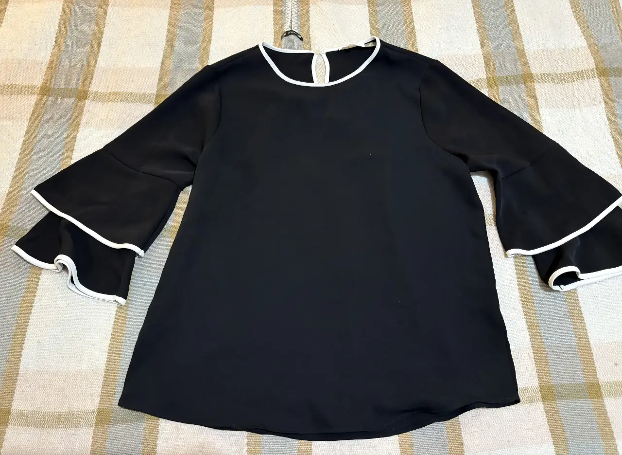 Blusa negra con mangas acampanadas y detalles en blanco. Ideal para un look elegante y versátil.