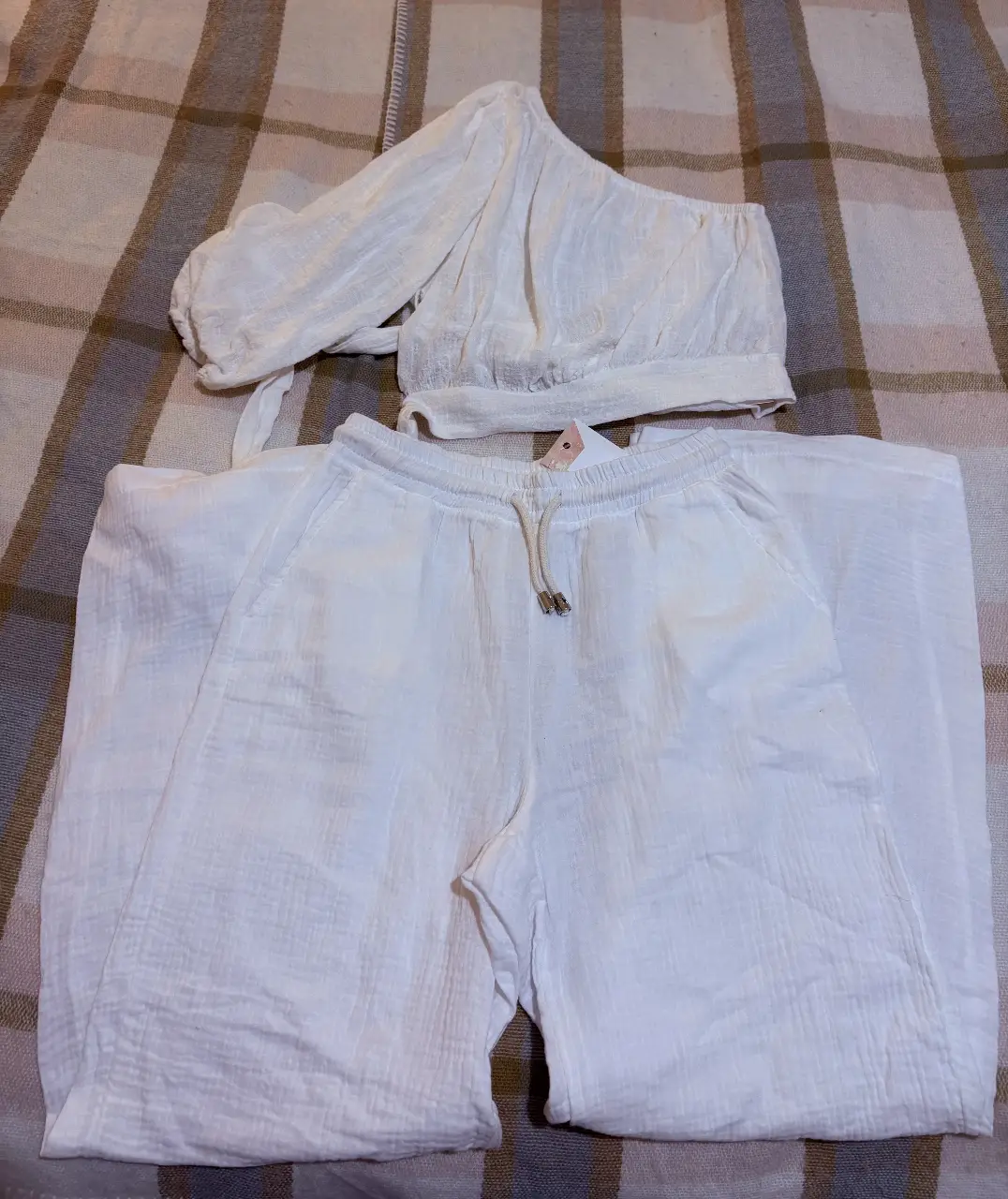 Conjunto de dos piezas blanco, ideal para el verano. Incluye un top asimétrico de manga larga y un pantalón suelto con cintura elastizada.