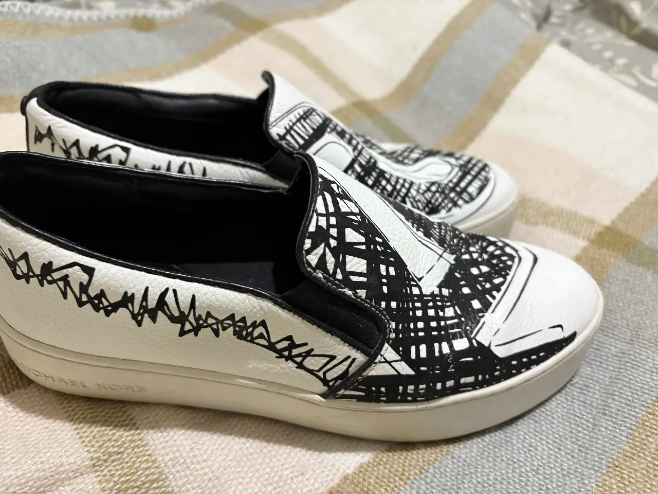Zapatillas slip-on Michael Kors blancas con detalles en negro. Diseño moderno y cómodo, ideales para un look casual y con estilo.