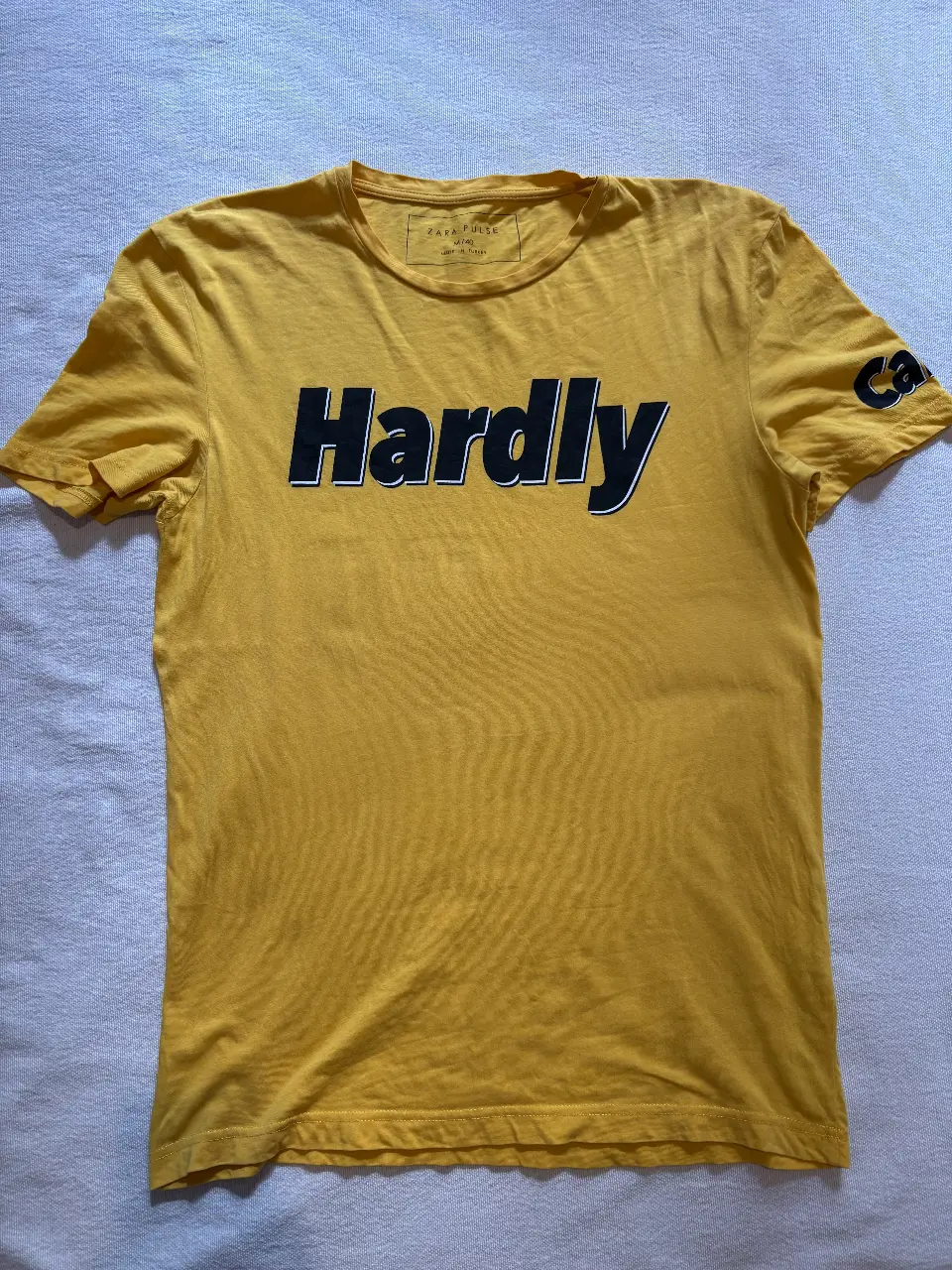 Remera amarilla de hombre con estampado "Hardly" en negro y blanco en el pecho. Manga corta y detalle "Card" en la manga izquierda. Ideal para un look casual y moderno.