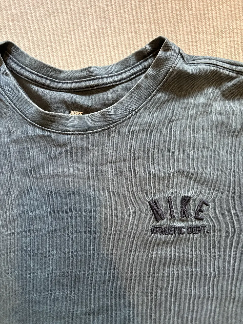 Remera Nike Athletic Dept. de hombre, color gris desgastado. Cuello redondo y logo bordado en el pecho. Ideal para un look casual y deportivo.