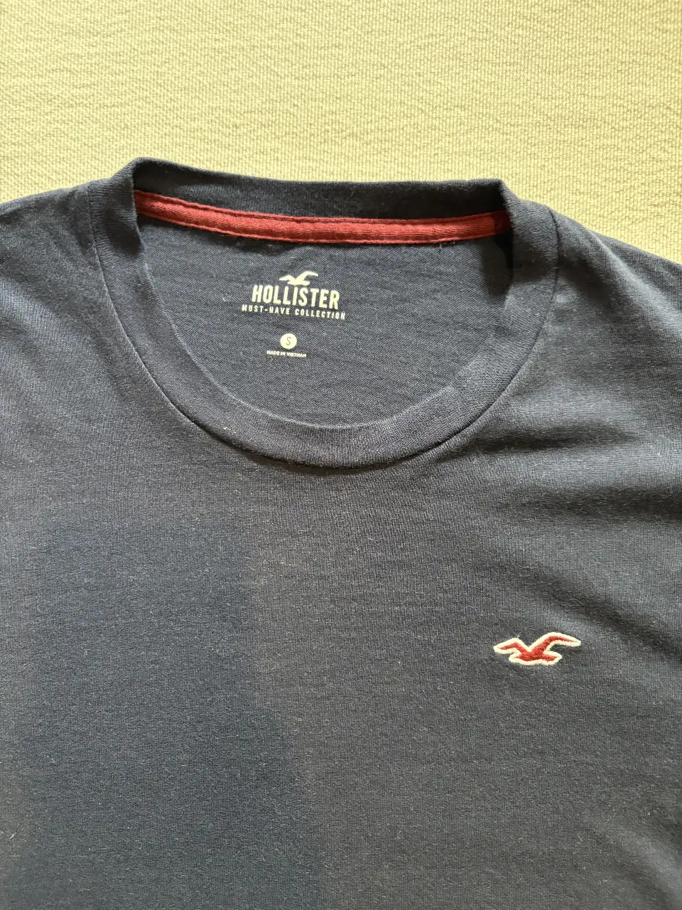 Remera de hombre Hollister azul marino, con logo bordado en el pecho. Cuello redondo con detalle en rojo. Must-have collection.