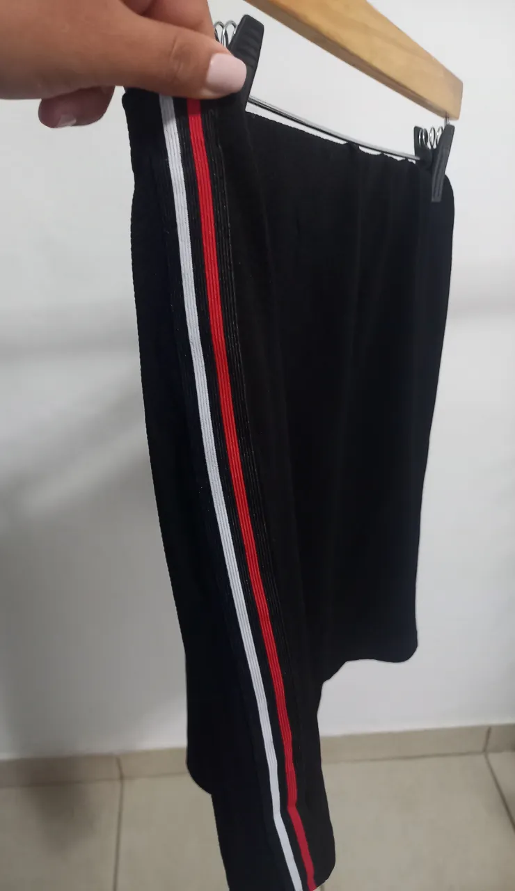 Pollera deportiva negra con franjas blancas y rojas en el lateral. Ideal para actividades físicas o un look casual.