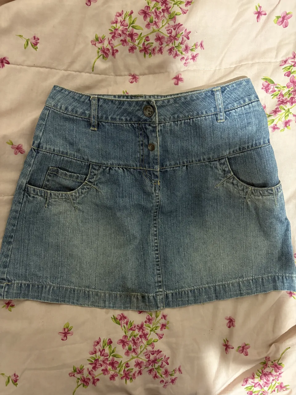 Pollera de jean tiro medio con bolsillos delanteros y traseros. Cierre con dos botones
