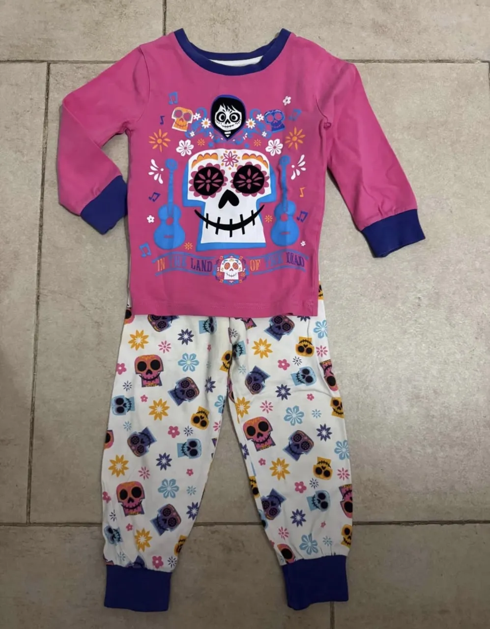 Pijama de dos piezas. La remera es manga larga, de color rosa con estampa de calaveras y guitarras. El pantalón es blanco con estampa de calaveras y flores.