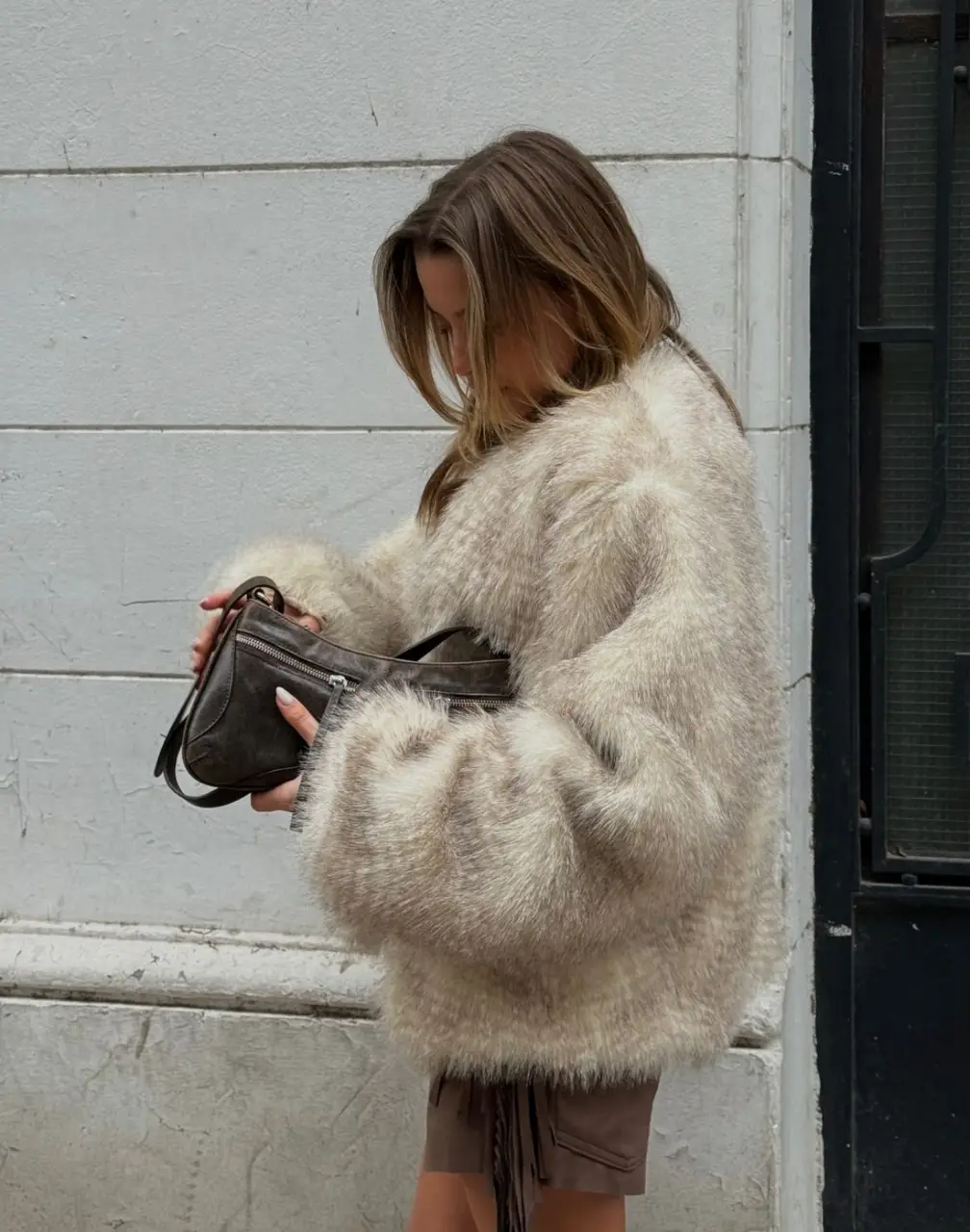 Abrigo de piel sintética en tonos crudos y marrones, ideal para un look de invierno. Con un diseño amplio y mangas largas, este tapado es perfecto para combinar con shorts y botas.