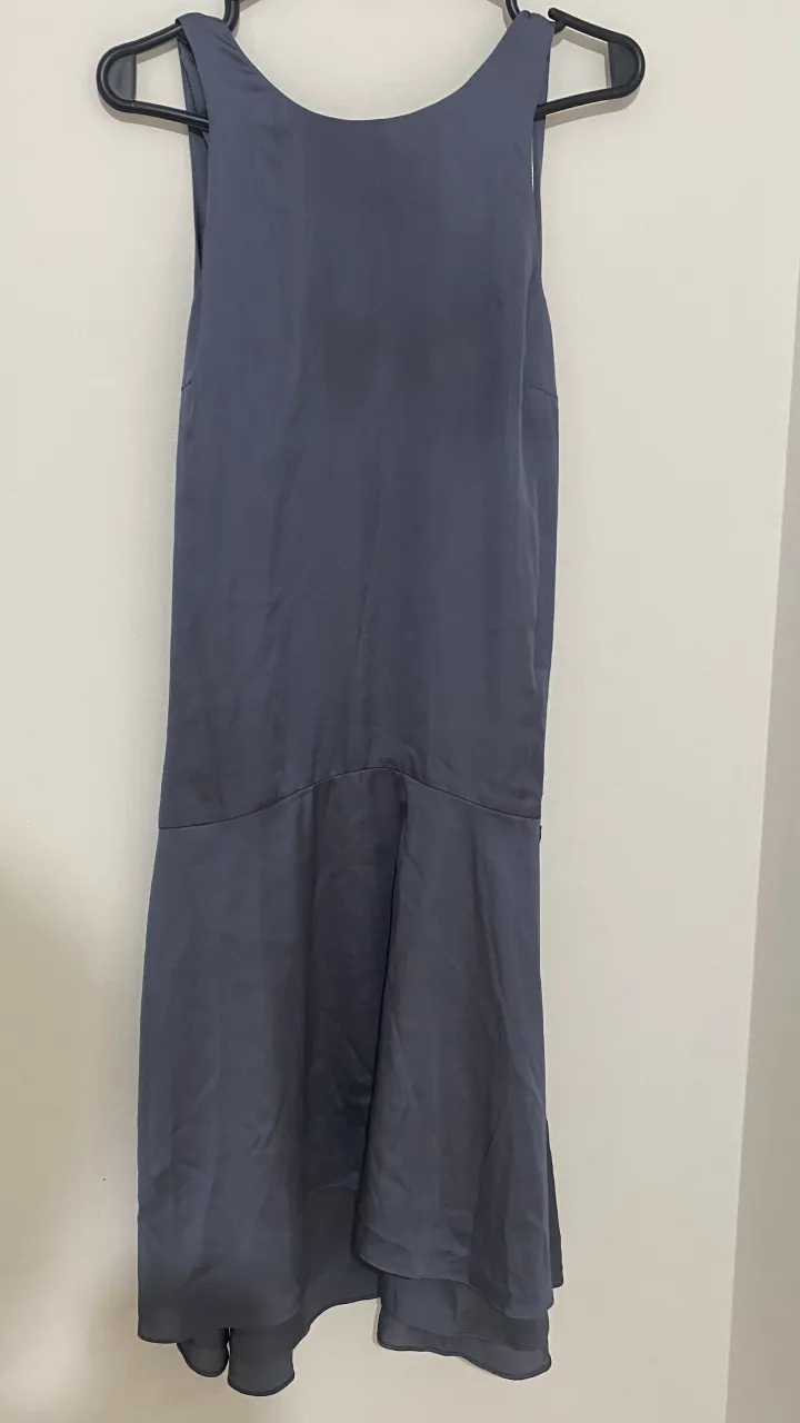 Vestido gris oscuro, largo hasta la rodilla, con un corte asimétrico y detalles en la falda. Ideal para eventos o salidas.