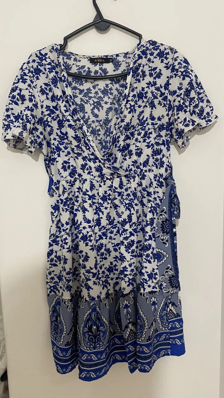 Vestido corto estampado floral en tonos blanco y azul. Posee escote cruzado y falda con detalles de guarda estampada en la parte inferior. Ideal para un look fresco y femenino.