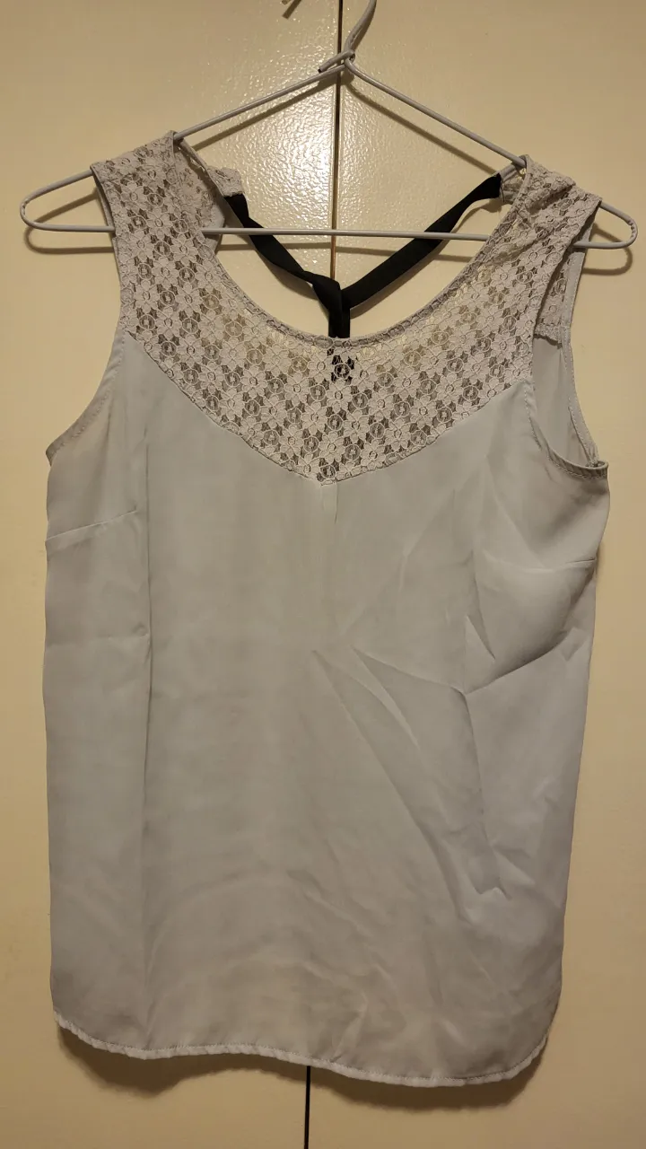 Top de seda gris con detalles de encaje en el escote y espalda. Posee un lazo negro en la nuca para atar. Ideal para un look canchero y elegante.