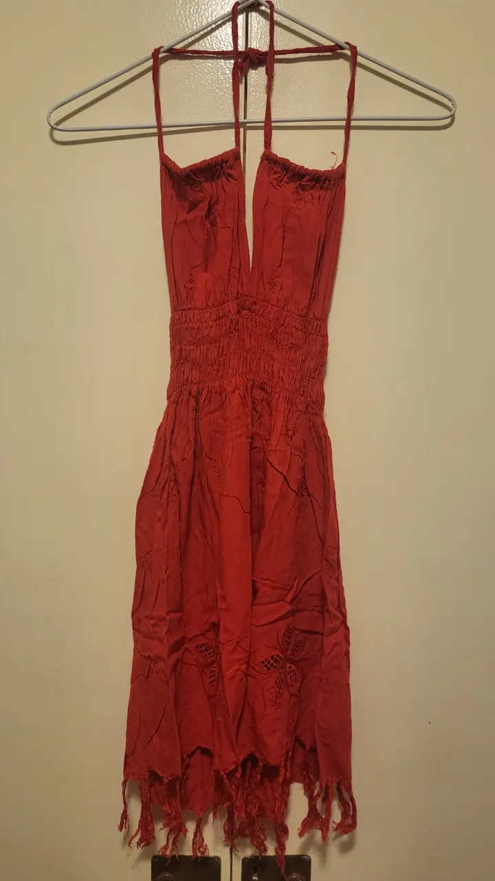 Vestido rojo de tela liviana, con escote halter y detalles de bordado y flecos en la parte inferior. Ideal para un look playero o de verano. También disponible en negro.