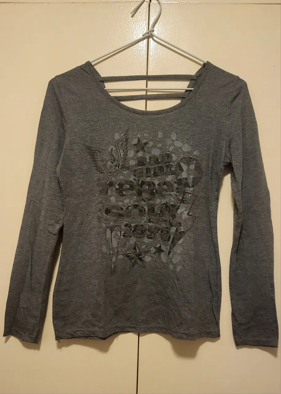 Remera gris de manga larga con un diseño estampado en la parte delantera y un detalle de tiras en la espalda. Ideal para un look casual y moderno.