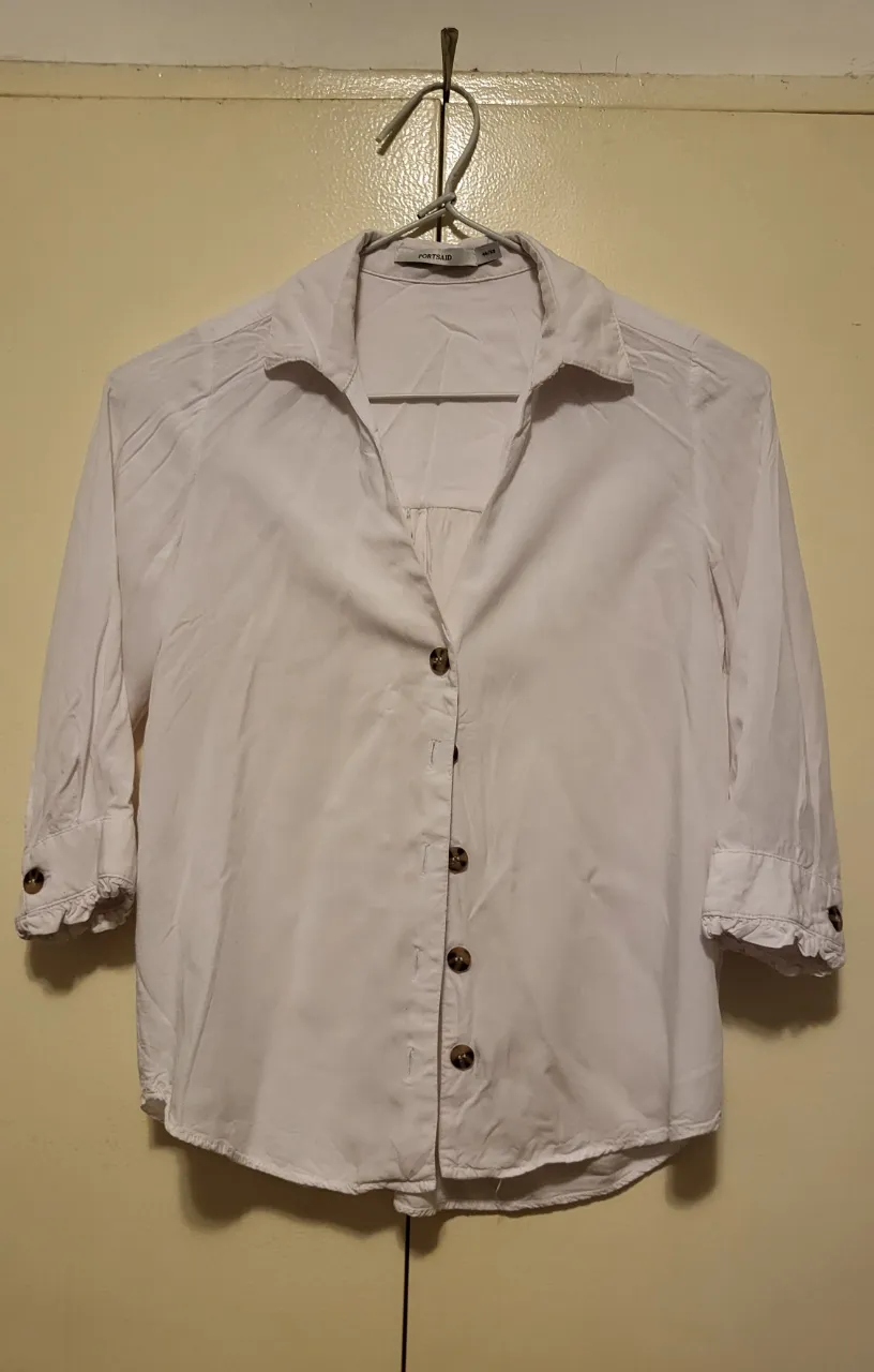 Camisa blanca de manga 3/4 con botones y detalles en los puños. Perfecta para un look casual o para ir a la oficina.