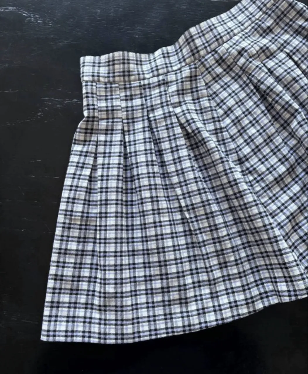 Pollera corta a cuadros escoceses en blanco, negro y celeste. Posee tabla encontrada en la parte delantera y cierre con un botón en la cintura.